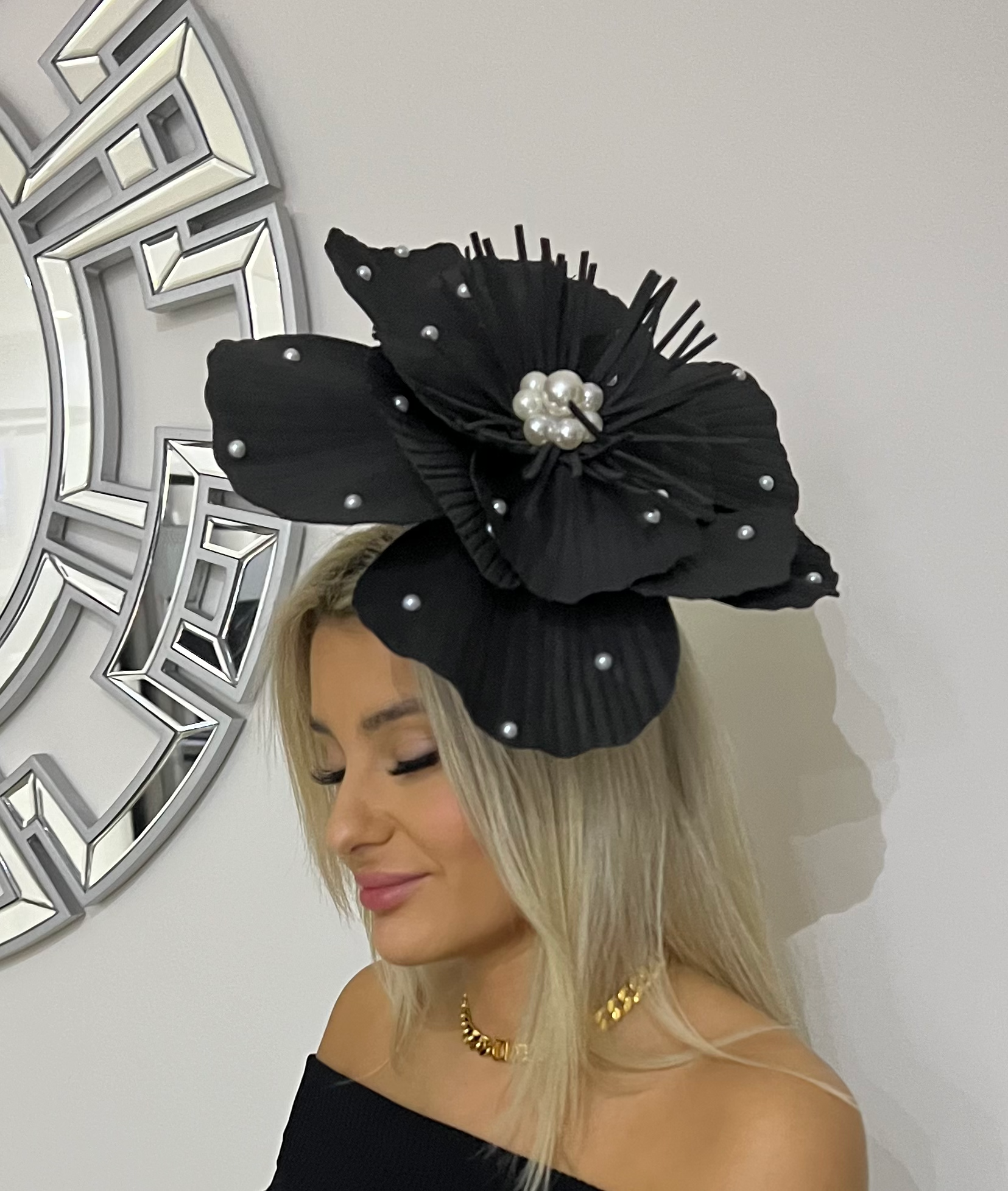Blonde woman in profile wearing a large black floral headpiece and gold necklace indoors
