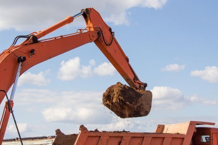 An Excavator Is Loading Dirt Into A Dump Truck — Sal's Excavations In St. Georges Basin, NSW