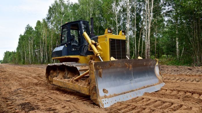 A Bulldozer Is Driving Down A Dirt Road In The Woods — Sal's Excavations In Vincentia, NSW