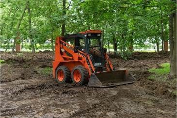 A Small Orange Bulldozer Is Driving Through A Muddy Field In The Woods — Sal's Excavations In Vincentia, NSW