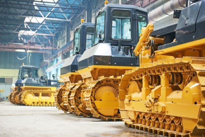 A Row Of Yellow Bulldozers Are Parked In A Warehouse — Sal's Excavations In Vincentia, NSW