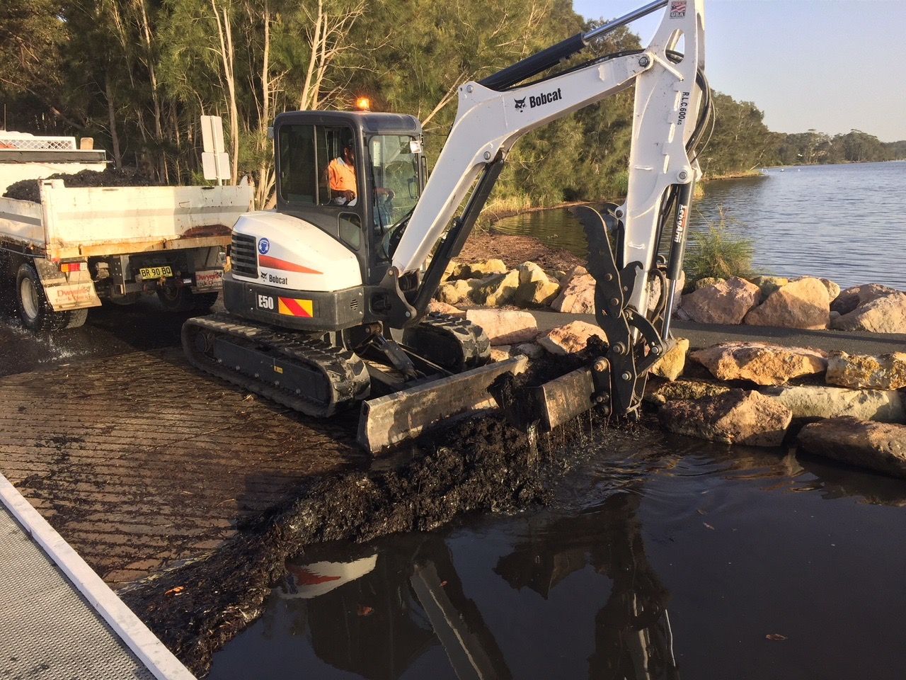 A Small Excavator Digging Waste In The Water — Sal's Excavations In St. Georges Basin, NSW