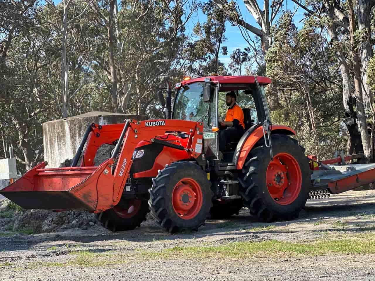 A Man Driving A Red Tractor With A Bucket Attached To It — Sal's Excavations In Falls Creek, NSW
