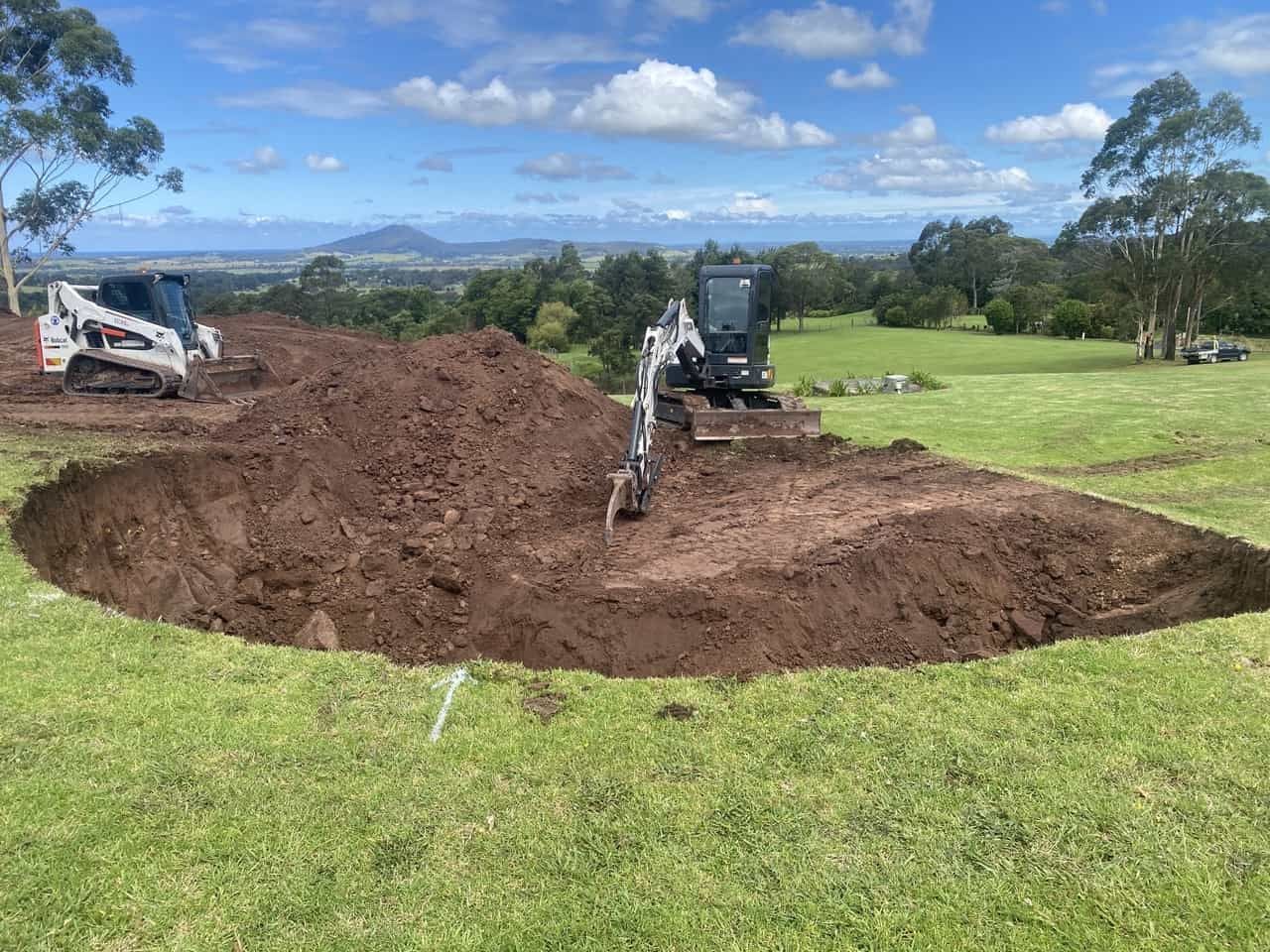 A Bulldozer Digging A Hole In The Ground In A Grassy Field — Sal's Excavations In Falls Creek, NSW