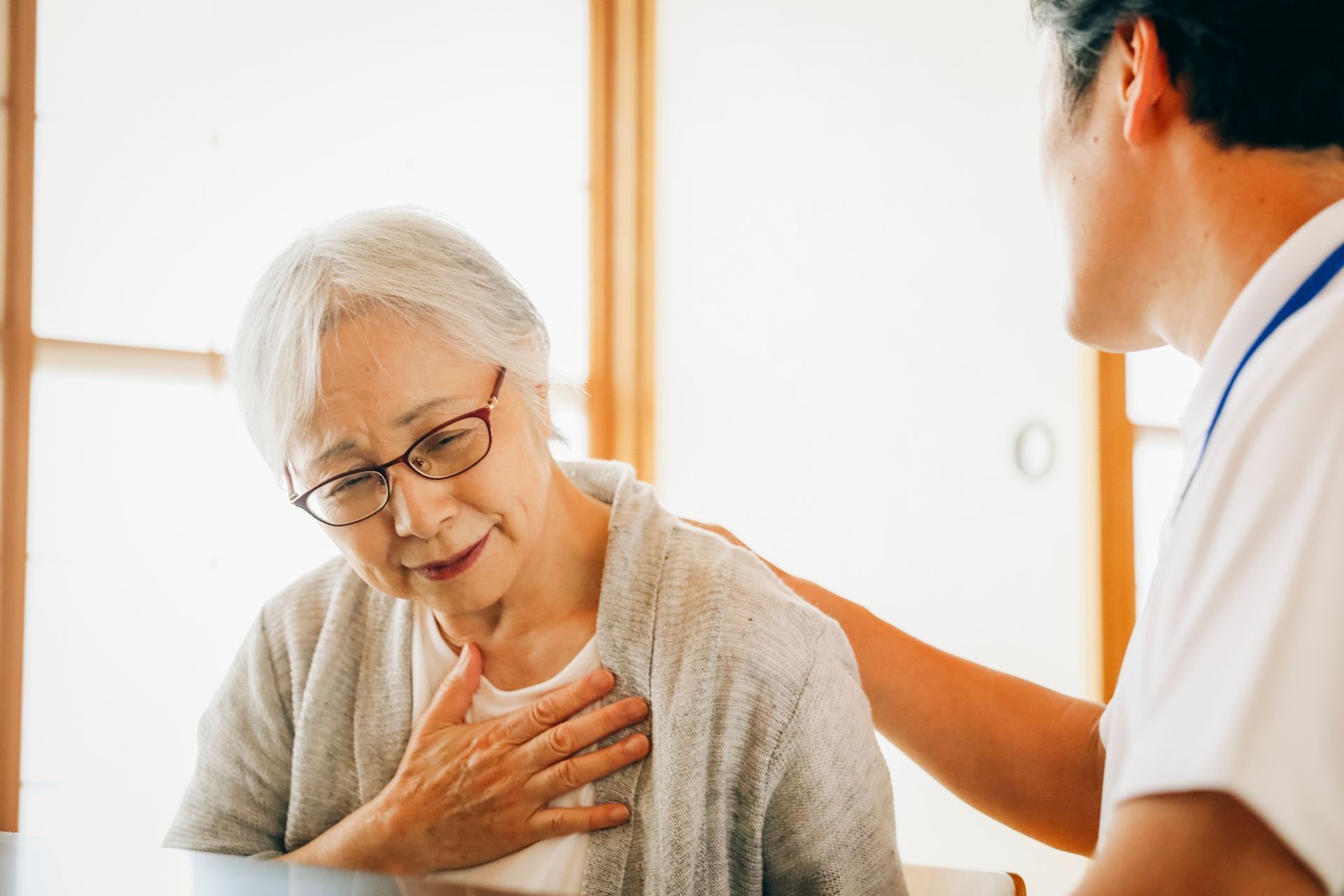 Healthcare worker comforting an elderly woman holding her chest in a bright room