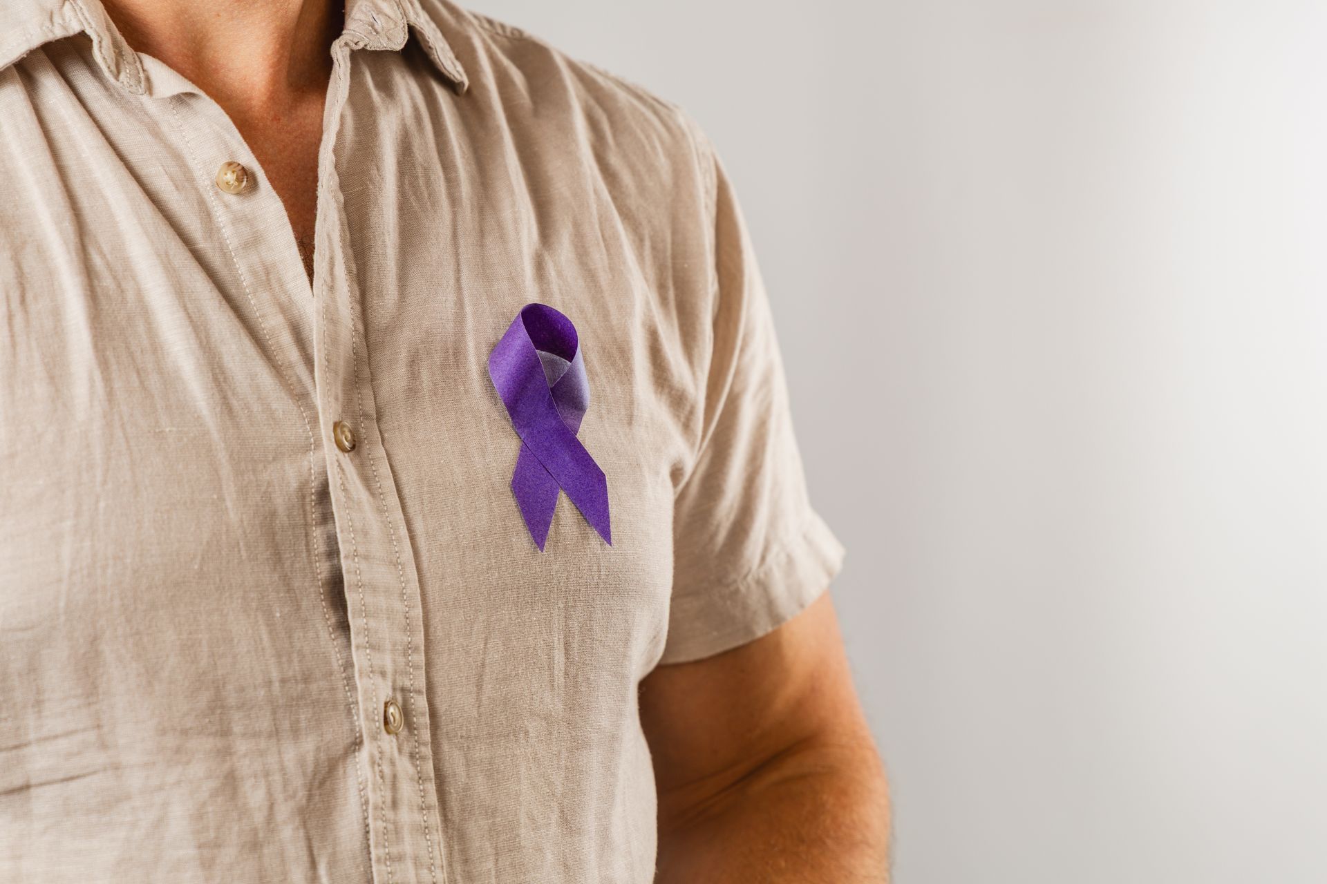 Shirted person with a purple awareness ribbon pinned to their chest