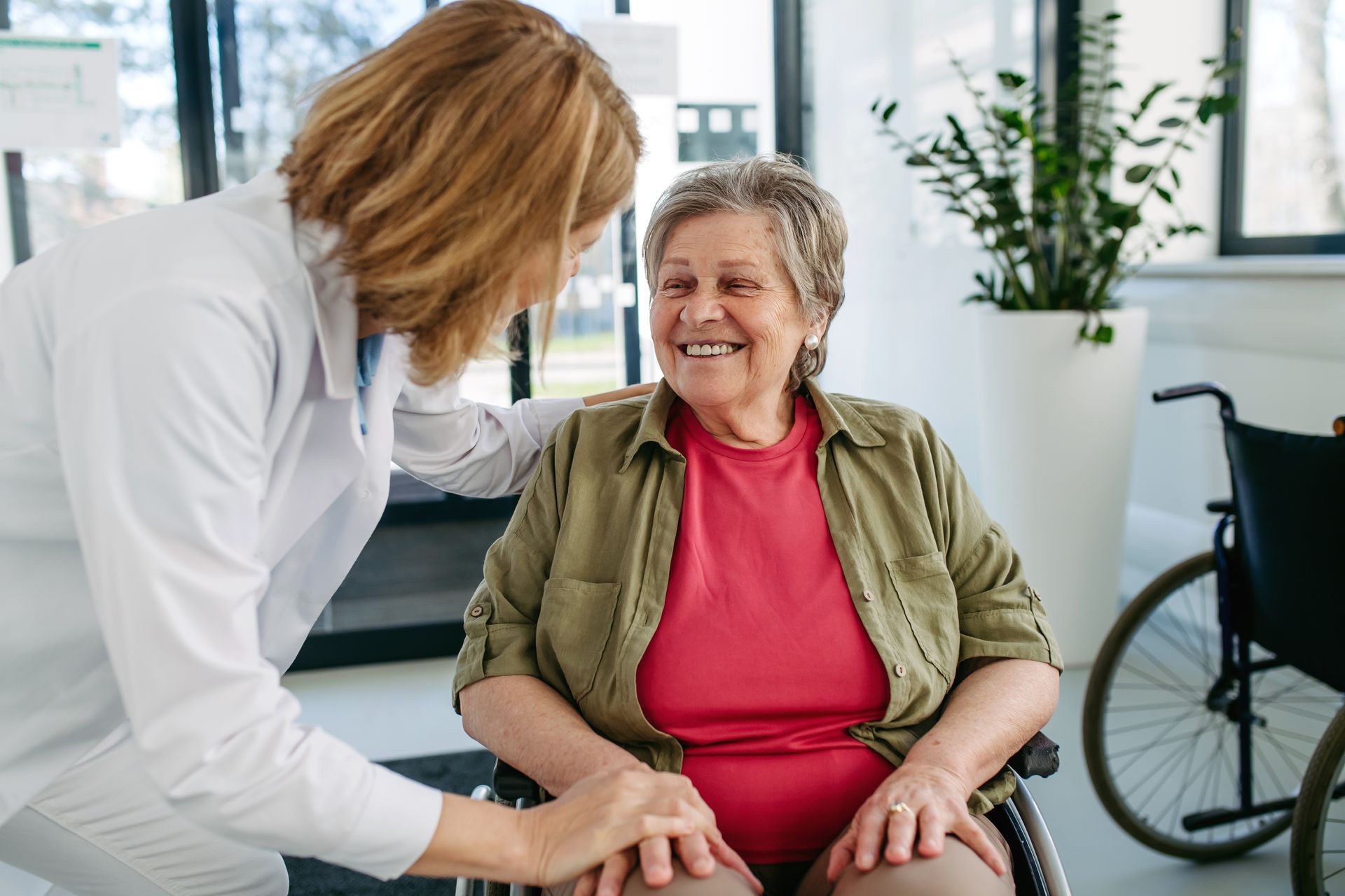 Caretaker helping a smiling wheelchair user in a bright clinic office