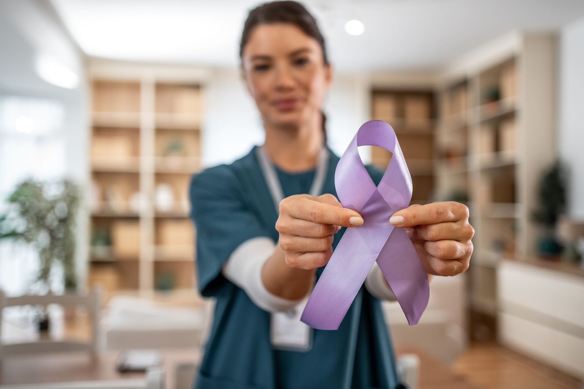 Woman holding a purple awareness ribbon in a blurred office setting