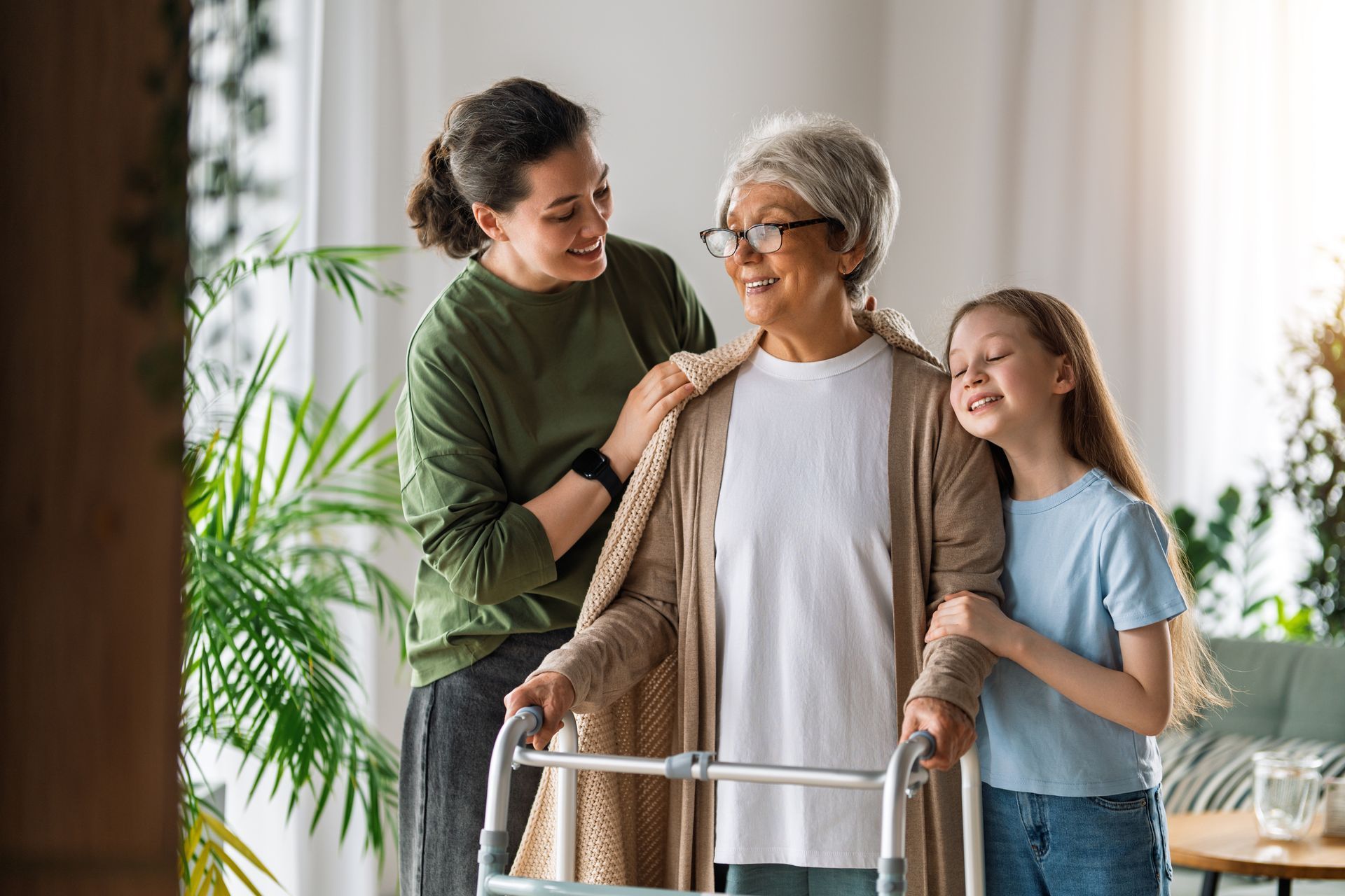 Senior woman using a walker with two smiling companions in a bright home interior