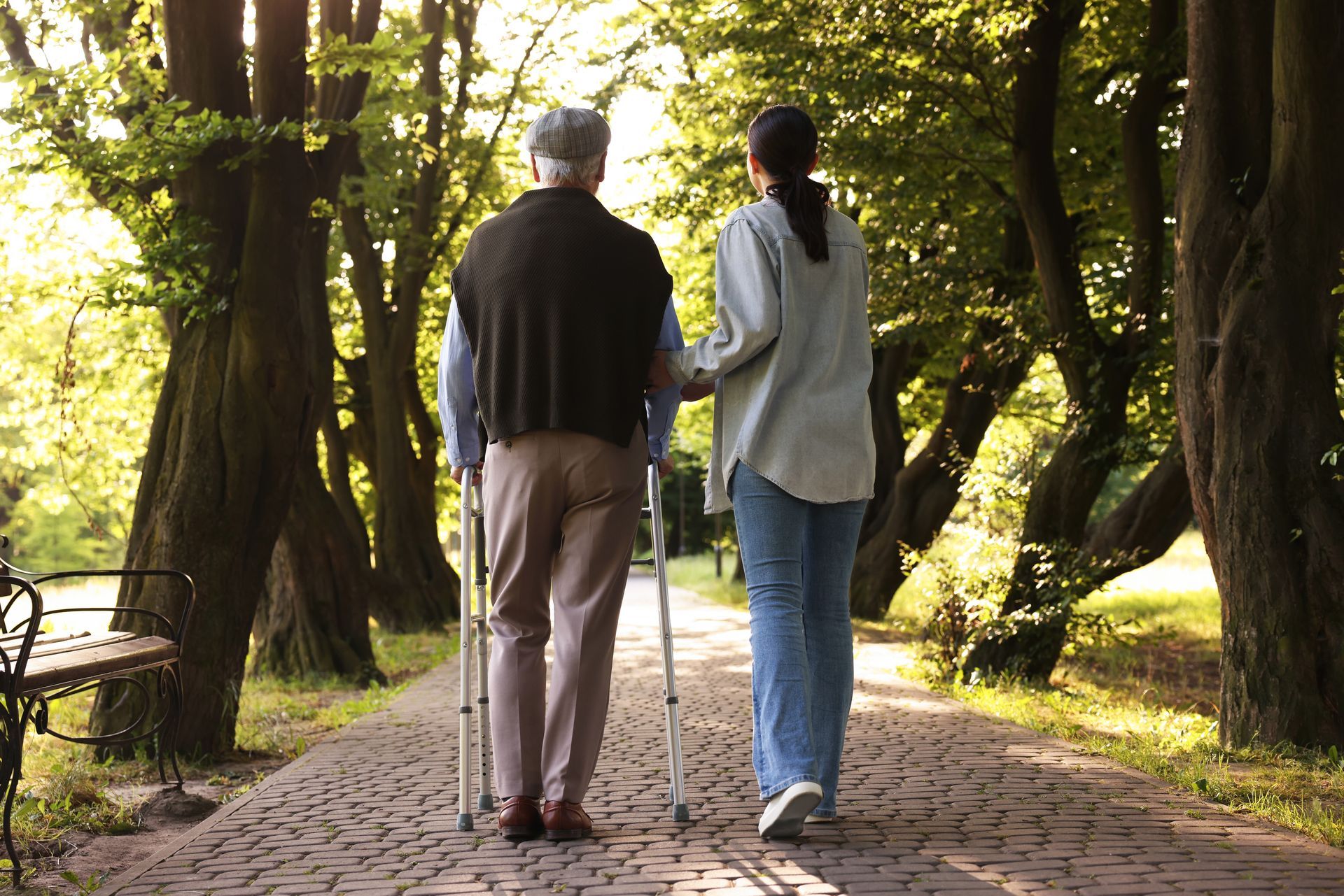 Two people walking on a tree-lined cobblestone path in a sunlit park