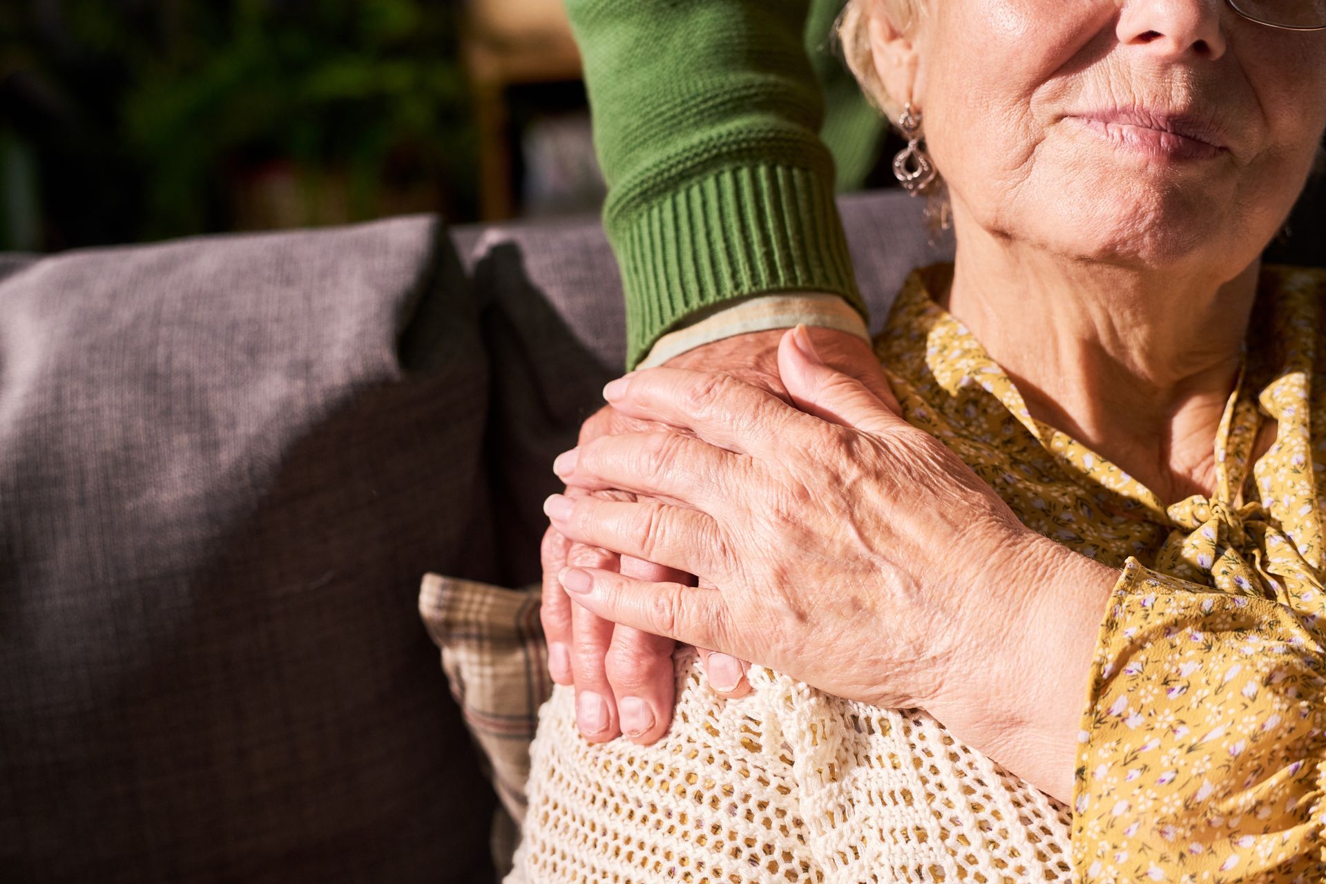 Hand on elderly woman’s shoulder in a cozy living room, offering comfort and support