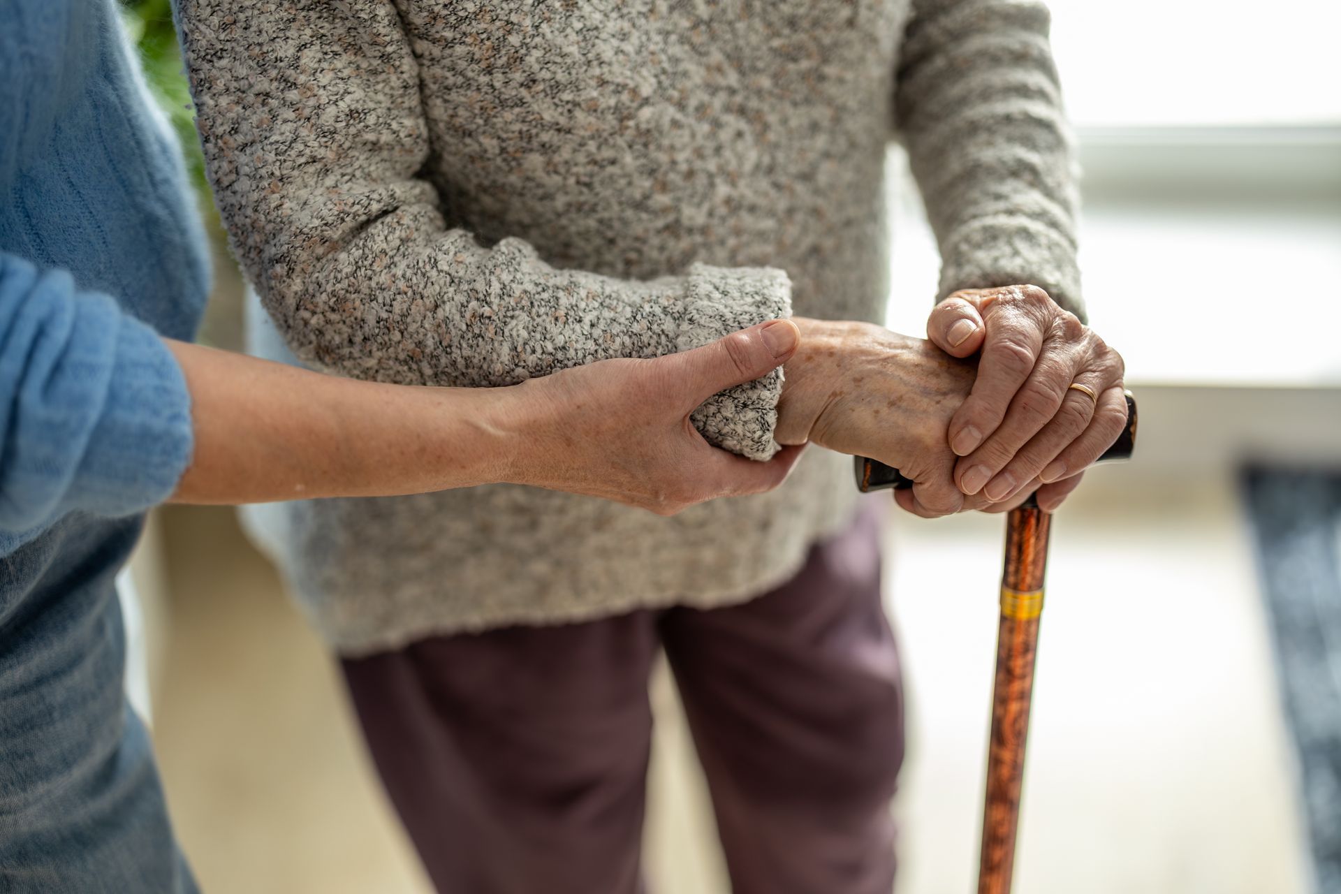Hands of two people, one holding a cane, showing support in a bright indoor setting