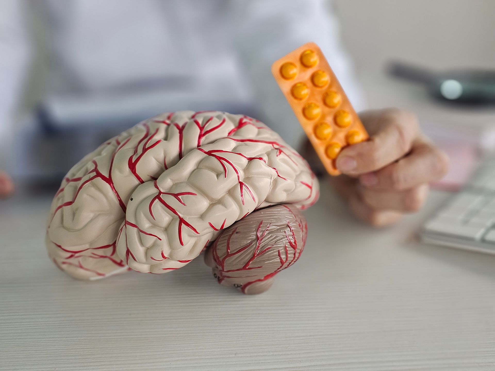 Brain model on desk beside a hand holding an orange pill blister pack