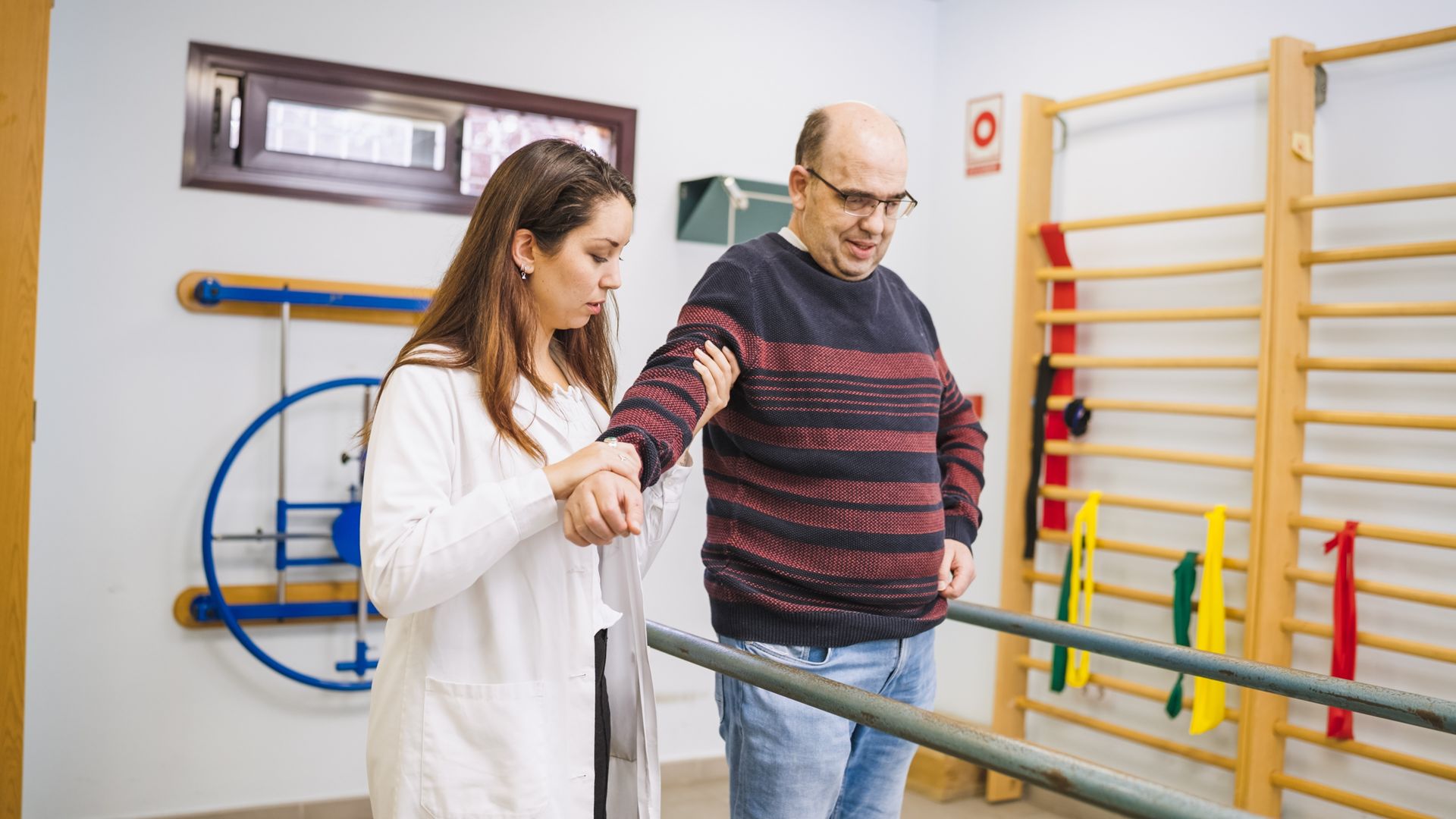Therapist assisting a patient on parallel bars during physical rehabilitation in a clinic
