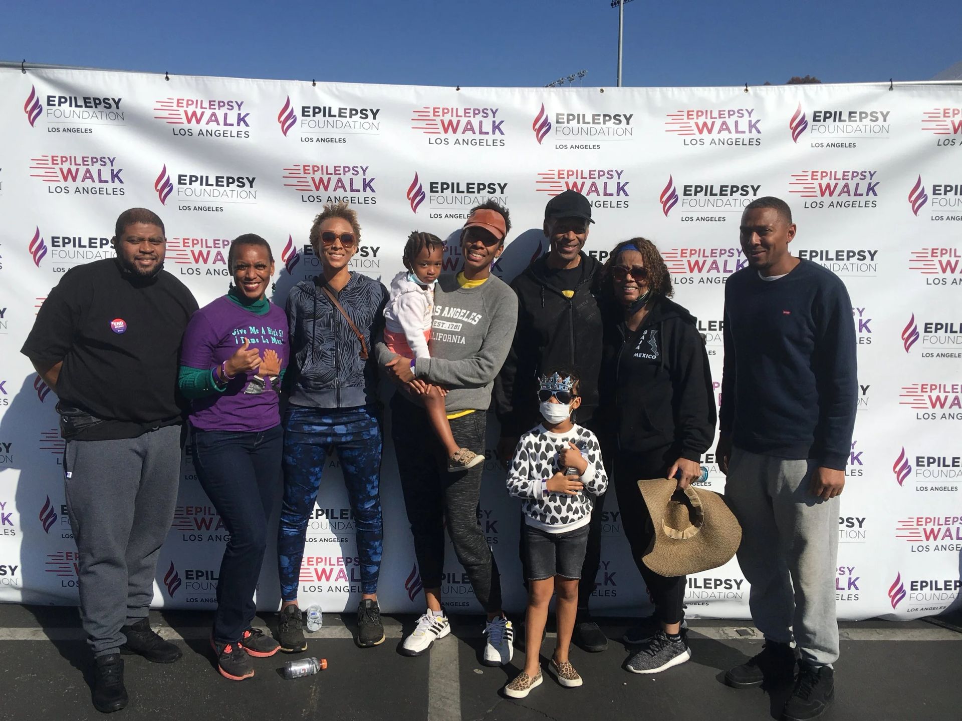 Group posing outdoors before a Walk event banner, with smiles and casual clothing