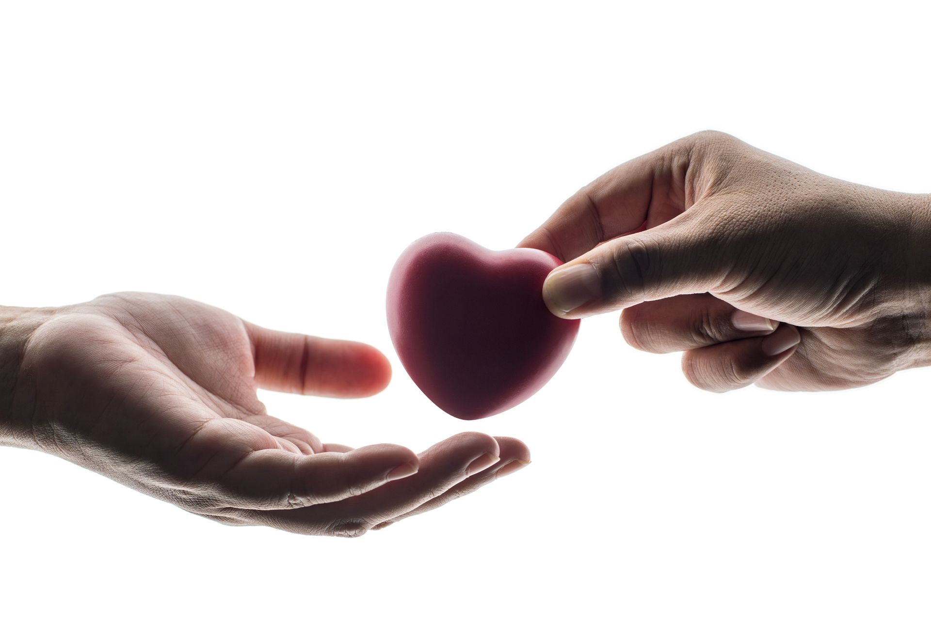 Two hands exchanging a small pink heart on a white background