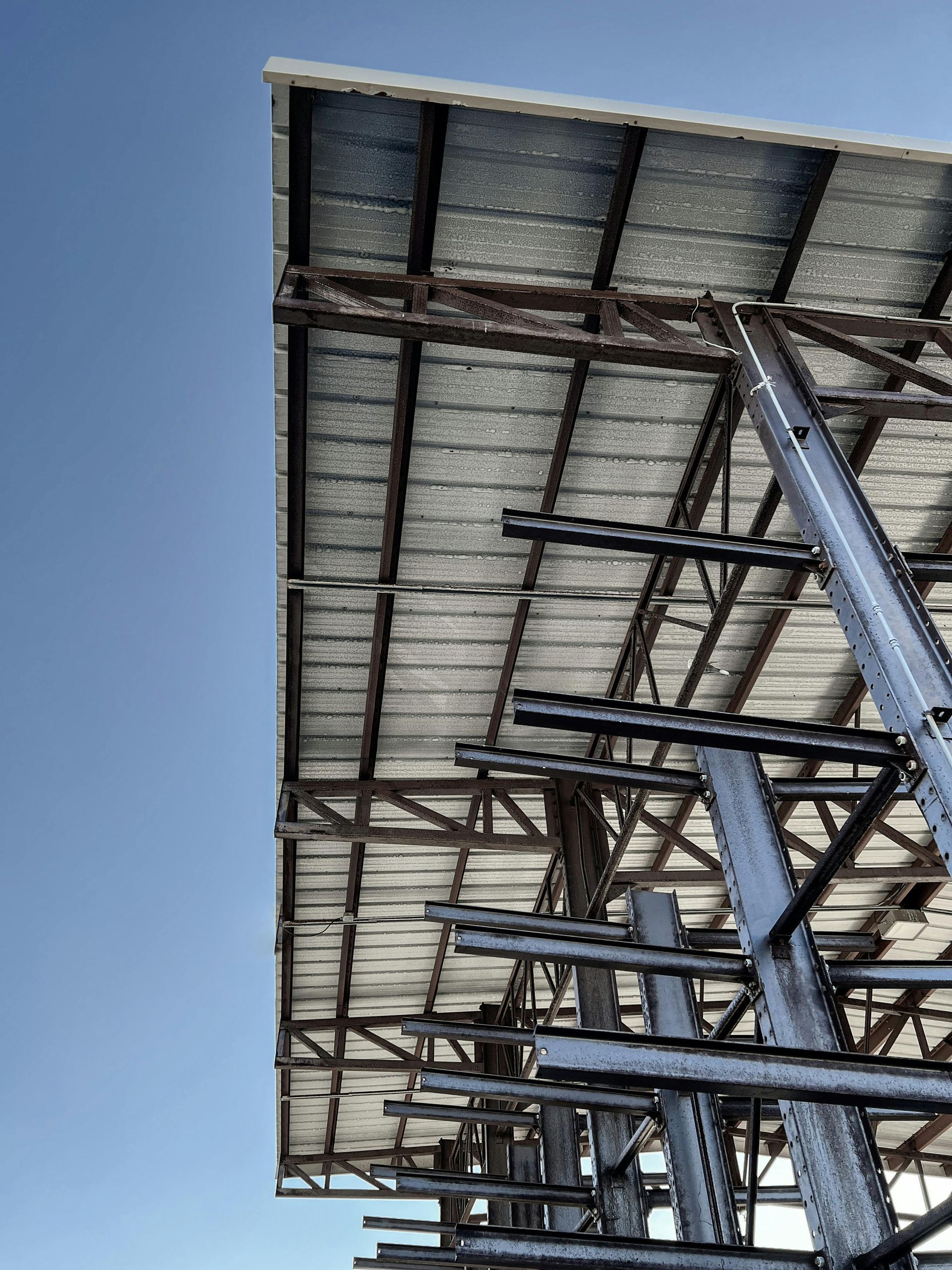 Underside of a steel-framed solar panel canopy against a clear blue sky