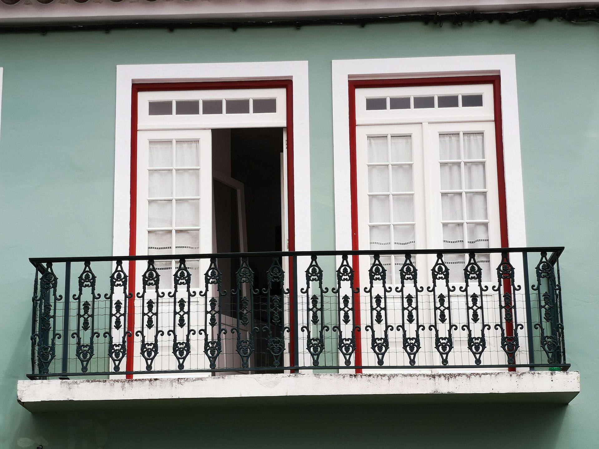 Open balcony with white shutters and black wrought-iron railing on a pale green building