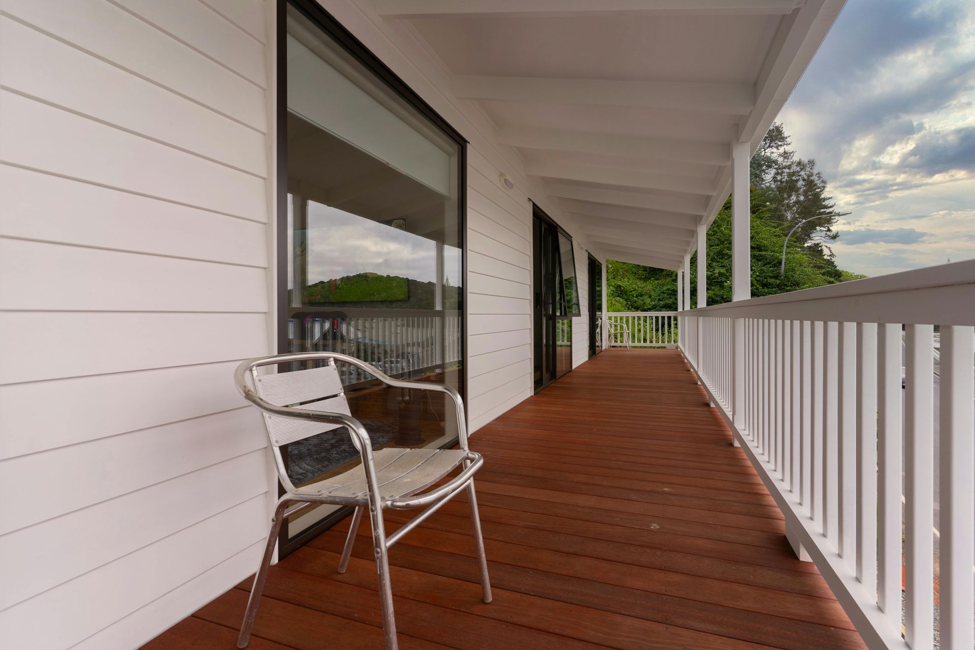 Covered wooden porch with white railing and a chair beside large windows