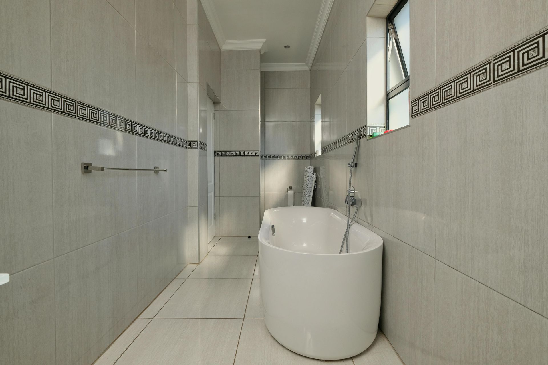 Narrow bathroom with a white freestanding tub, tiled walls, and a wall-mounted towel bar