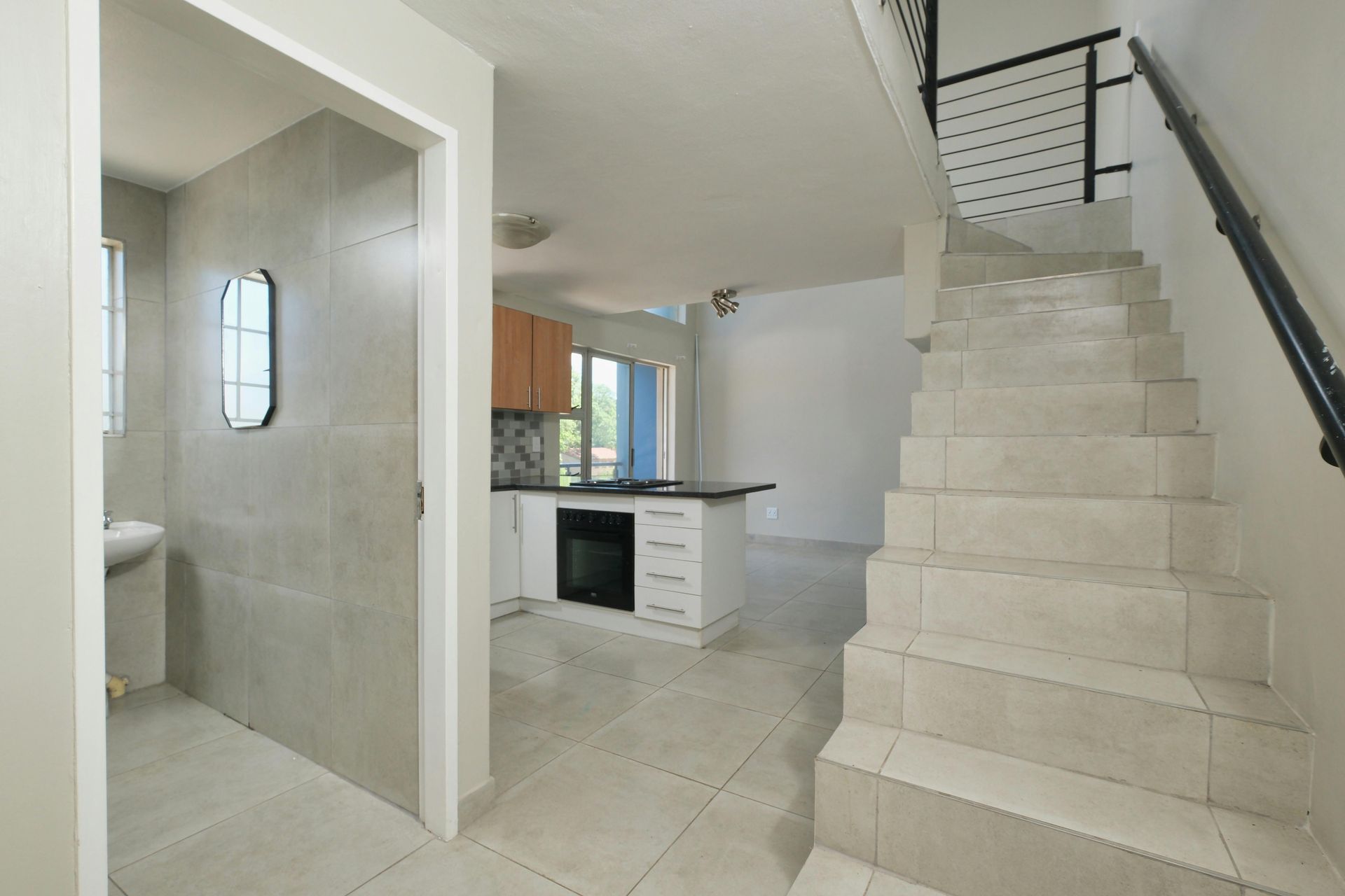 Interior stairway beside a small kitchen and tiled bathroom in a bright, white home