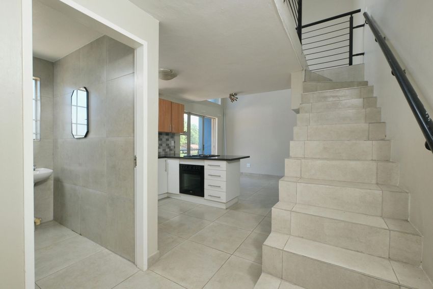Empty tiled foyer with stairs, kitchen, and a small bathroom visible through an open doorway.