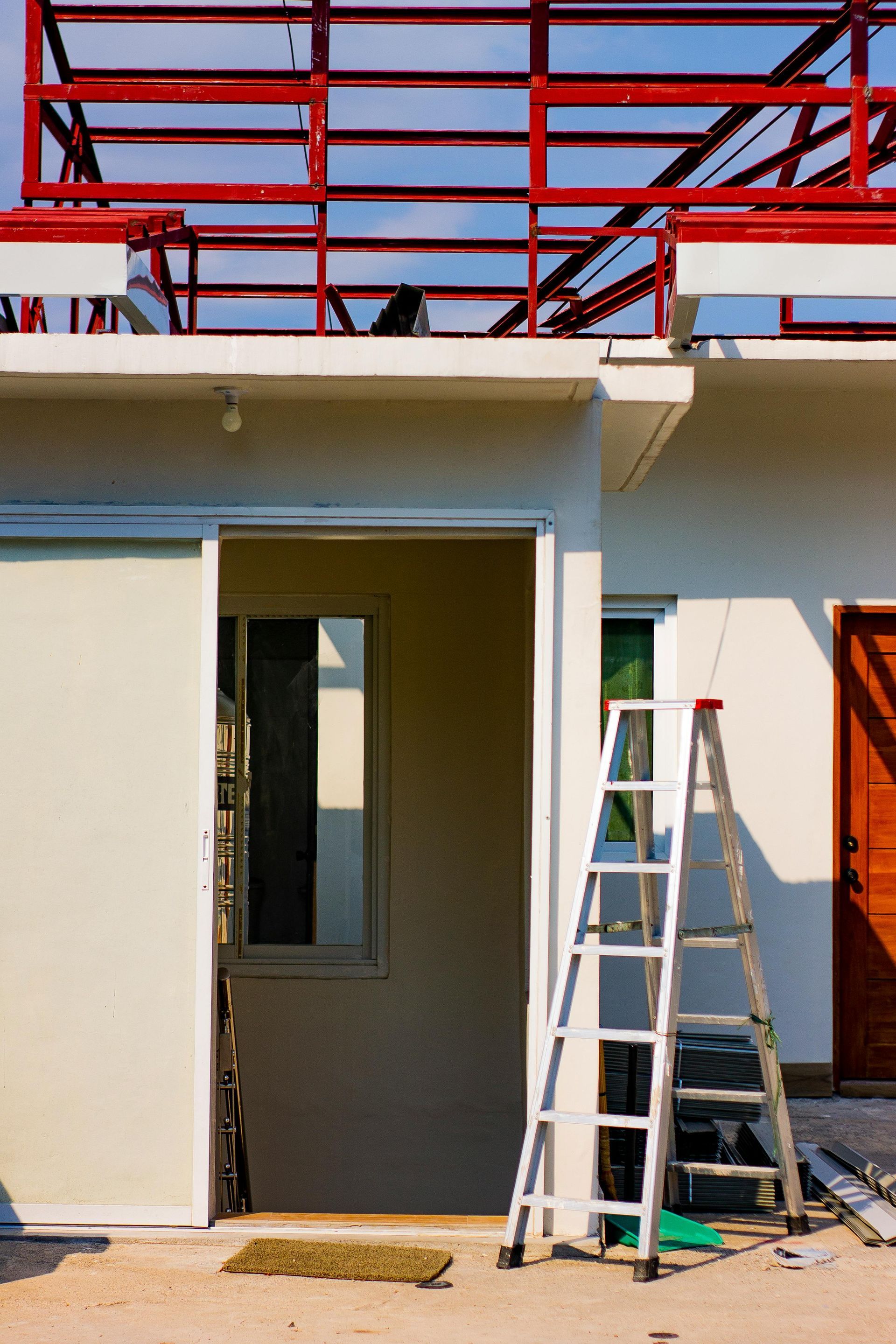 Two ladders beside a doorway on a building under construction, with red scaffolding overhead.
