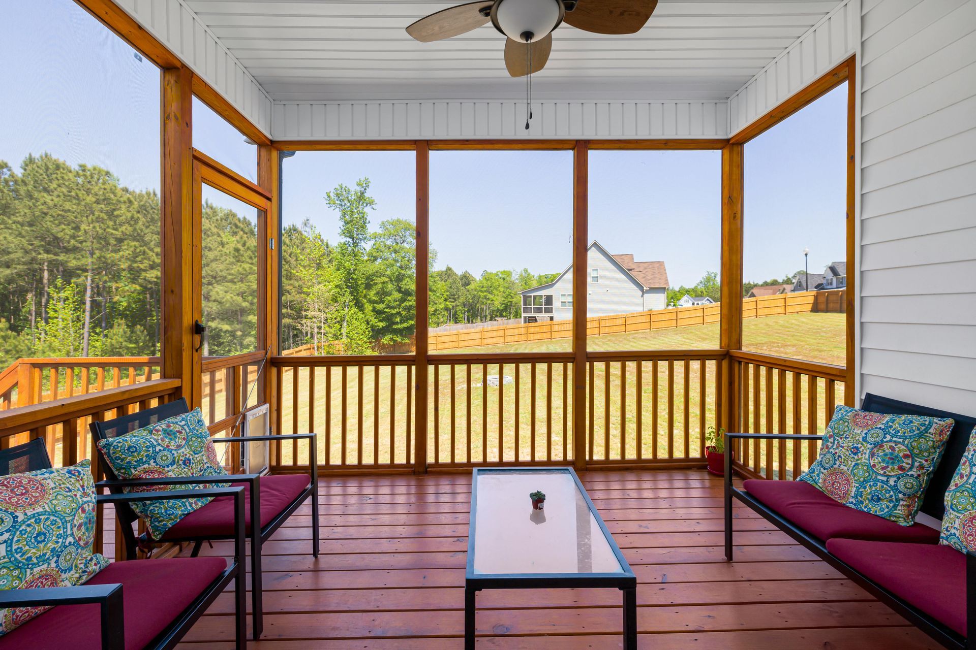 Covered porch with red floor, wicker chairs, glass table, and a view of trees and rooftops