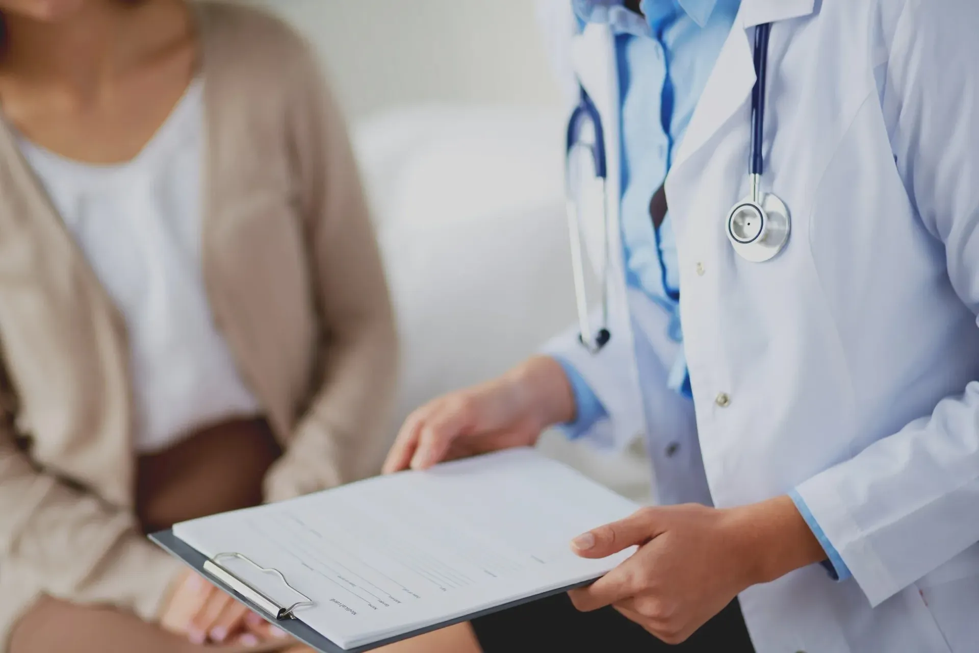 Doctor holding a clipboard with patient seated beside, in a clinic setting