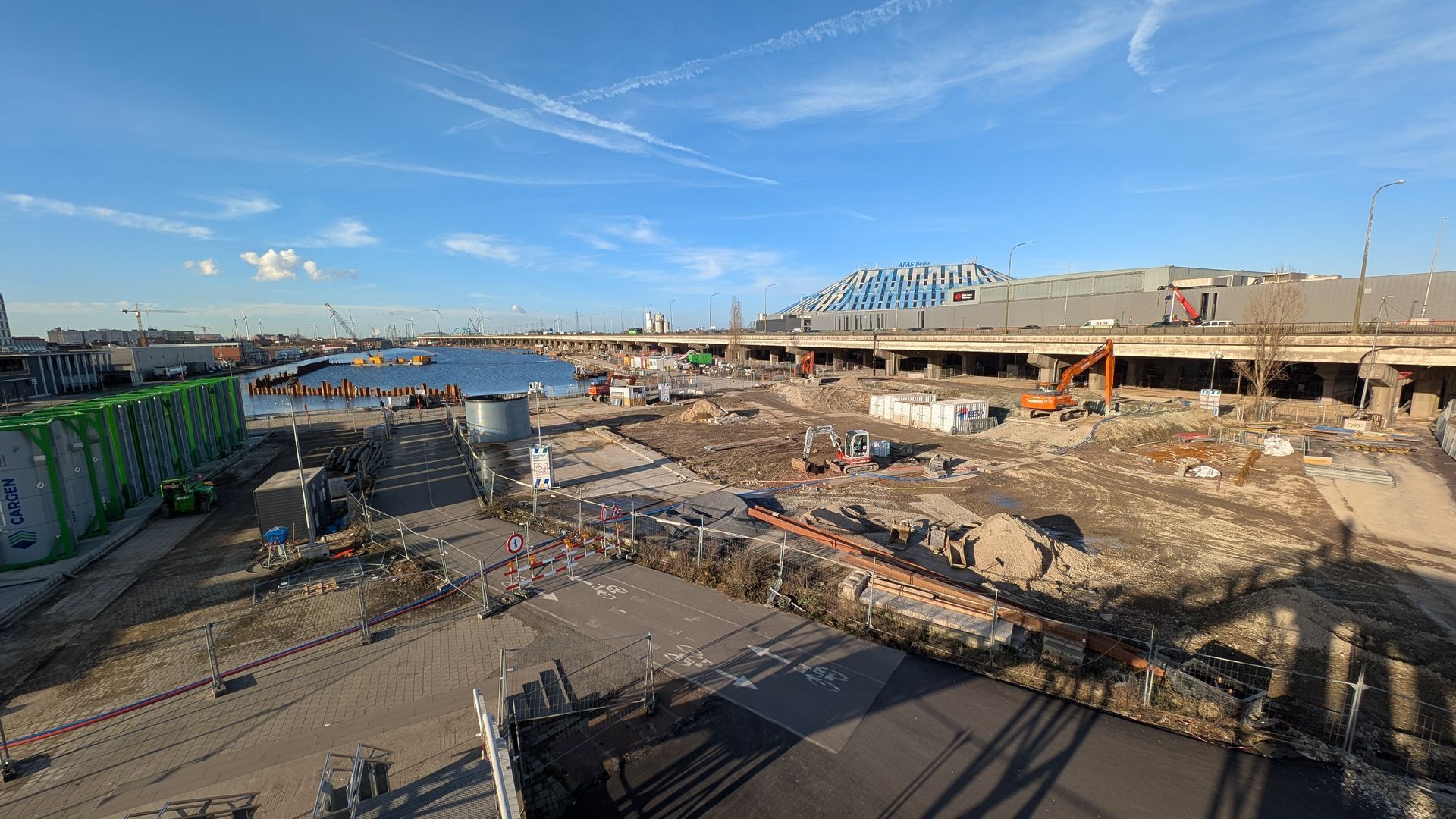 Construction site near water with blue sky and bridge in the background.