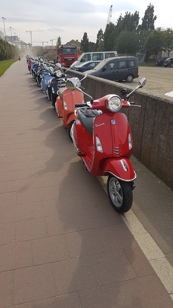 Row of colorful scooters parked along a paved walkway next to a stone wall.