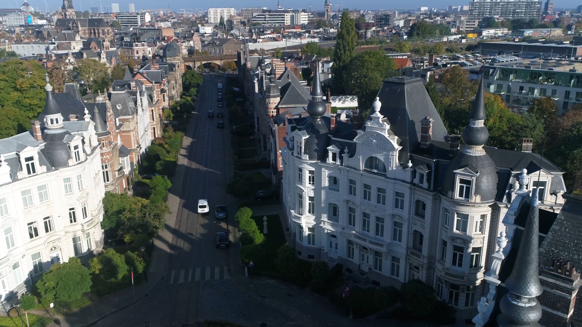 Aerial view of a European city street with ornate buildings, trees, and cars on the road.