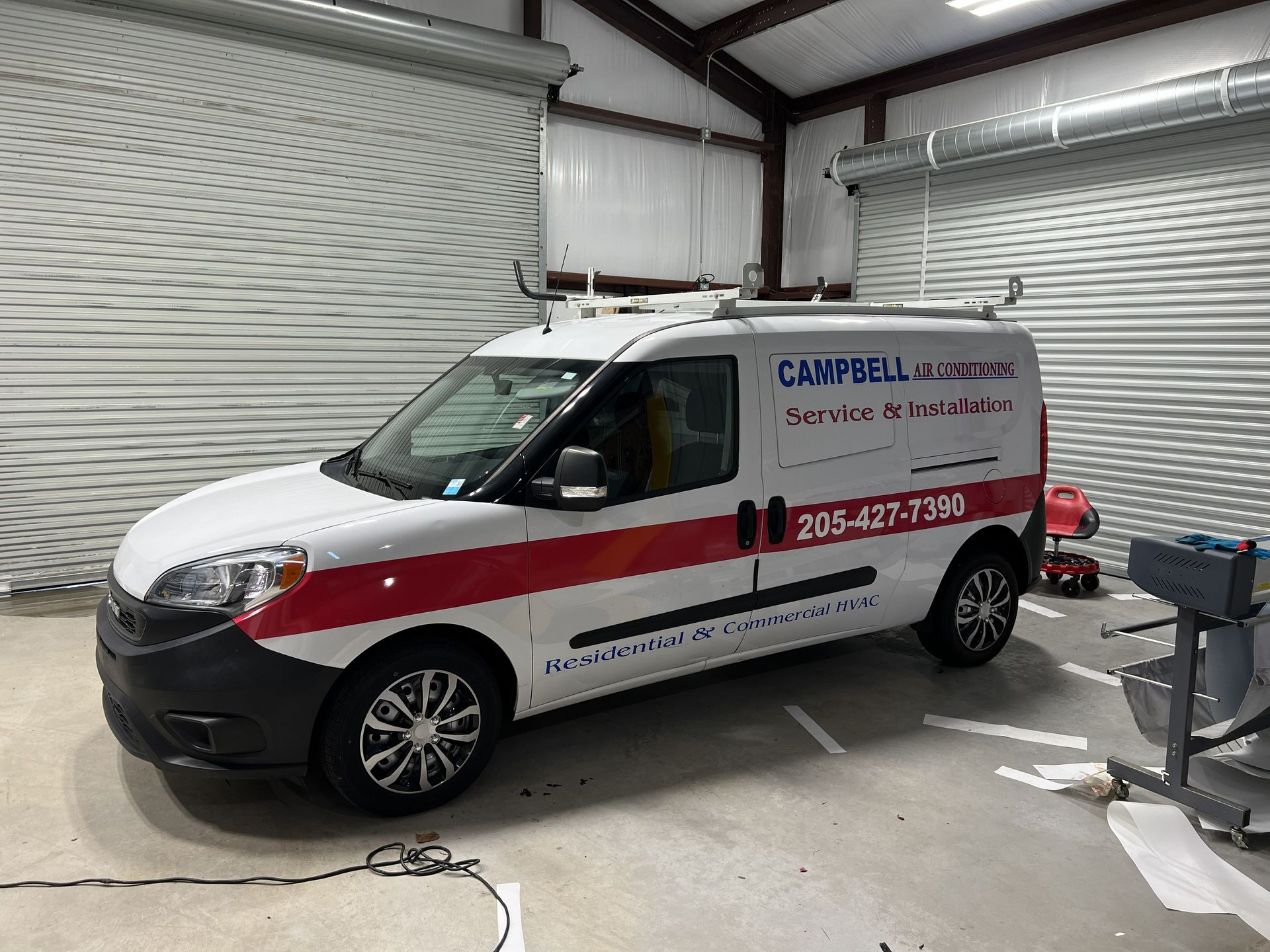 White service van with red stripe and business logo parked inside a garage.