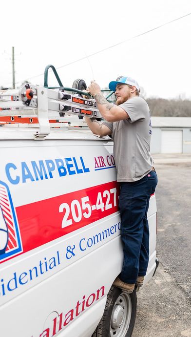Man in cap and grey shirt on van, working on top rack. 
