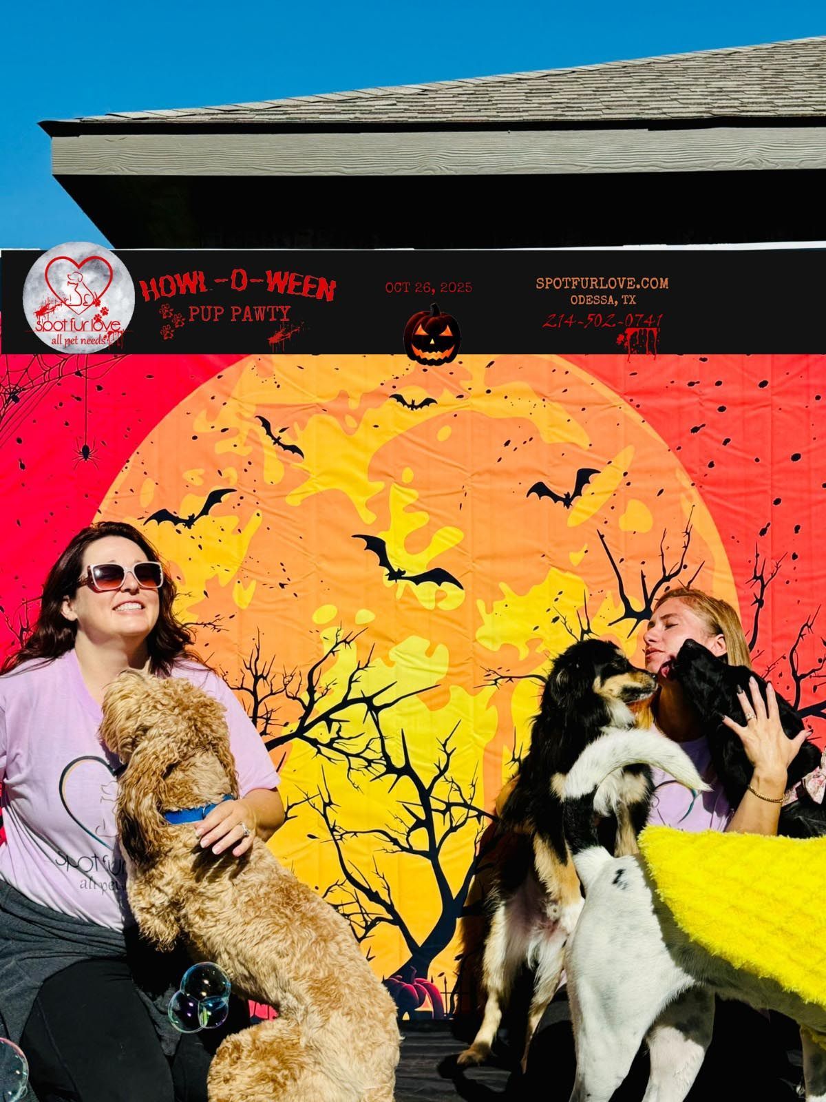 Two women with dogs in front of a Halloween backdrop with a full moon and bats.