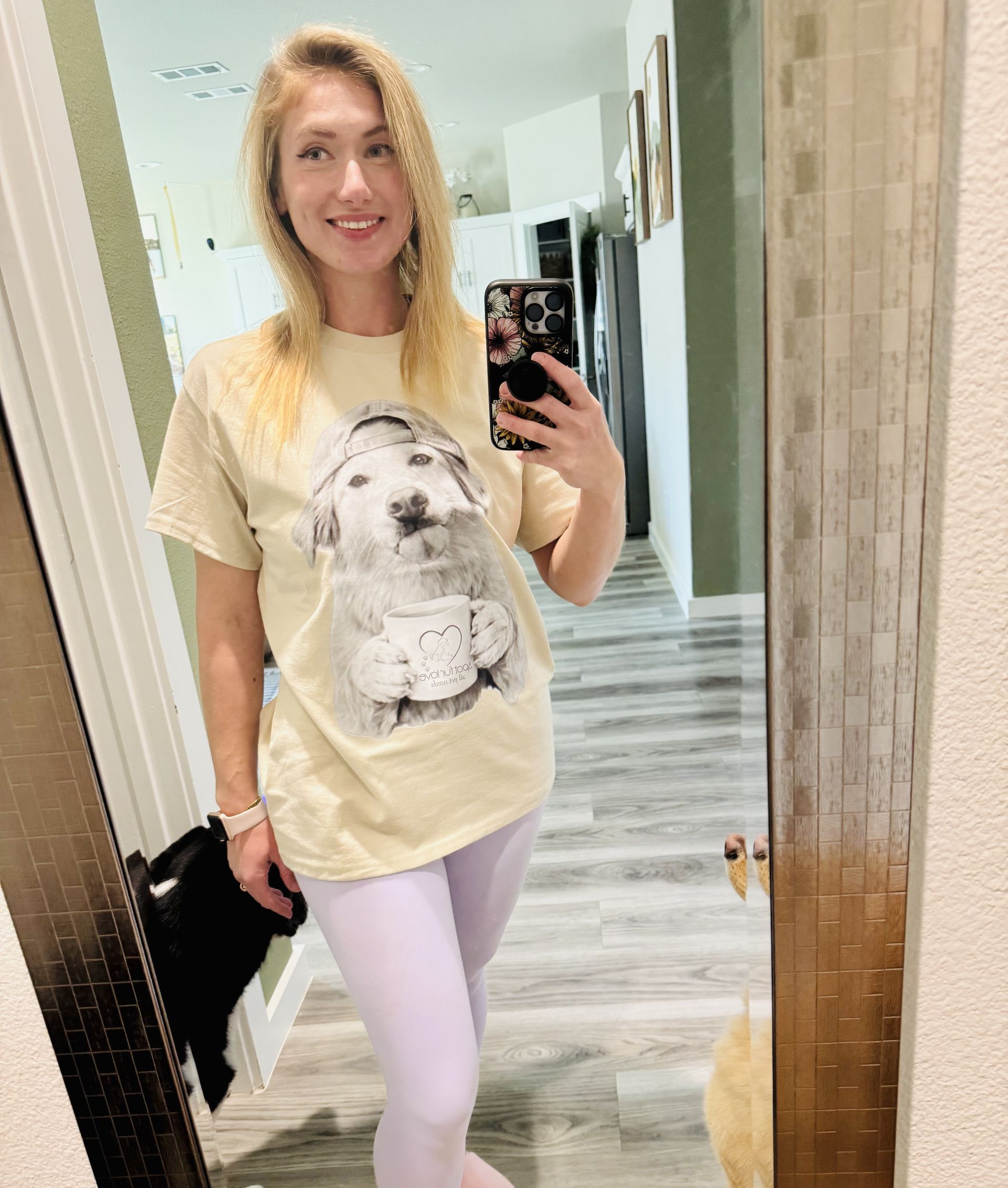 Woman in t-shirt with dog graphic, light purple leggings, taking a mirror selfie.