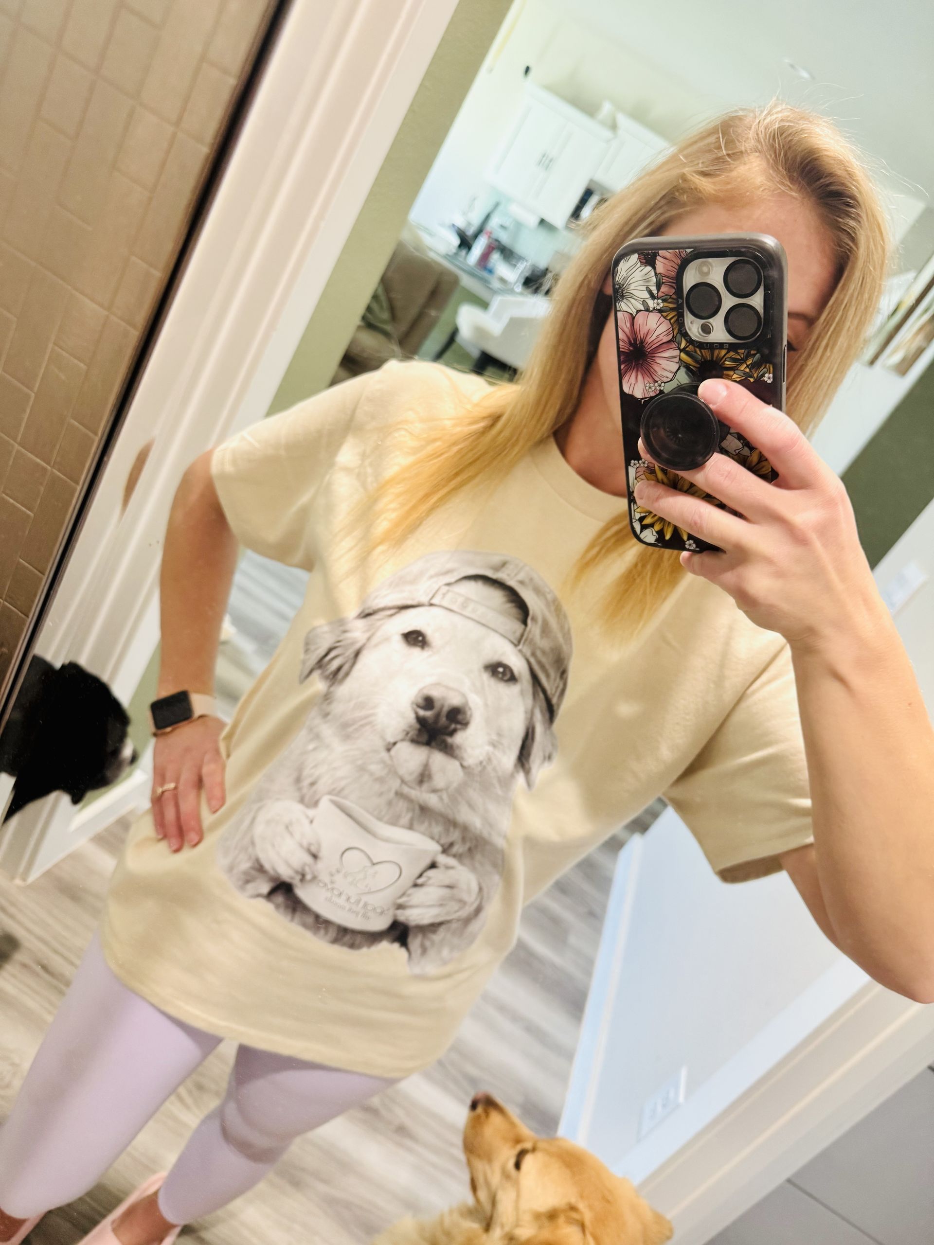 Woman wearing a dog graphic t-shirt and light purple leggings taking a selfie, dog in foreground.