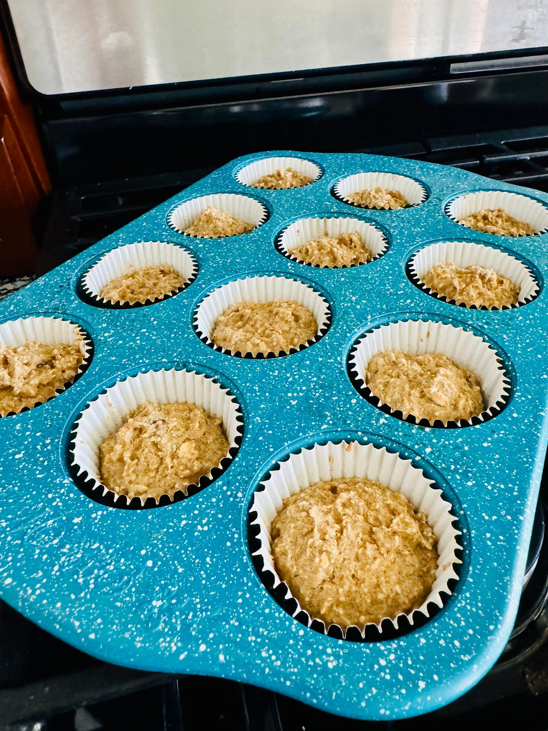 Muffin batter in white-lined cupcake tins, baking in a blue speckled muffin tin in an oven.