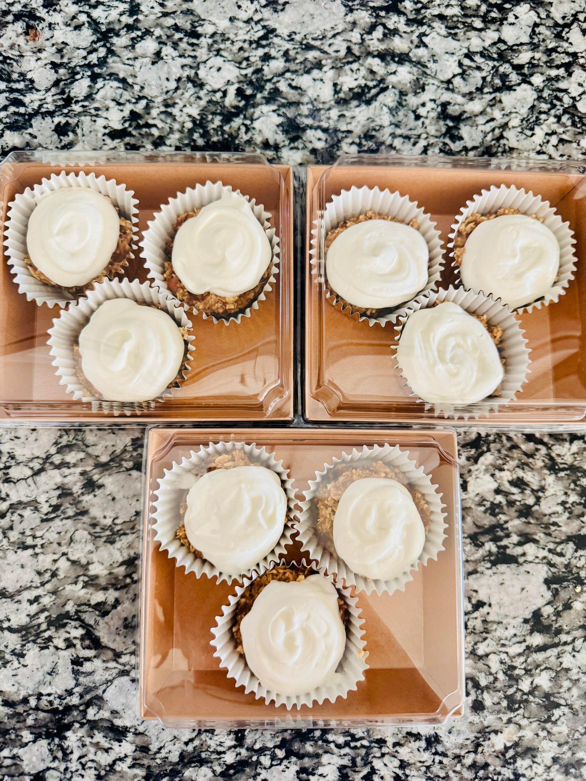 Three square boxes with six frosted cupcakes each, atop a marble countertop.