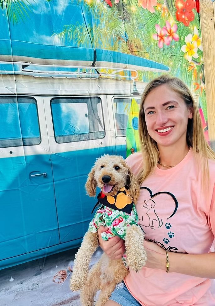 Woman holding a dog in front of a colorful mural of a van. Both are smiling.