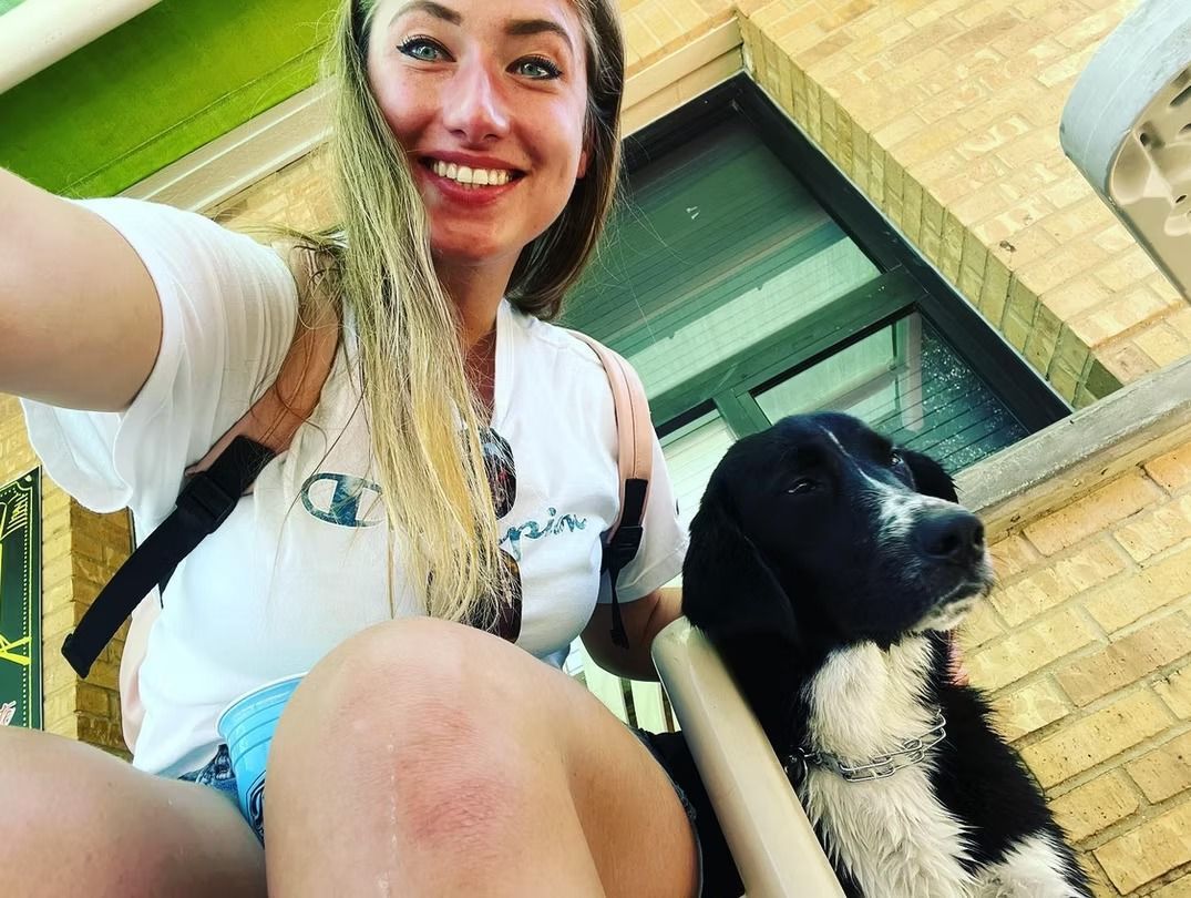 Woman smiles, poses with black and white dog outdoors.