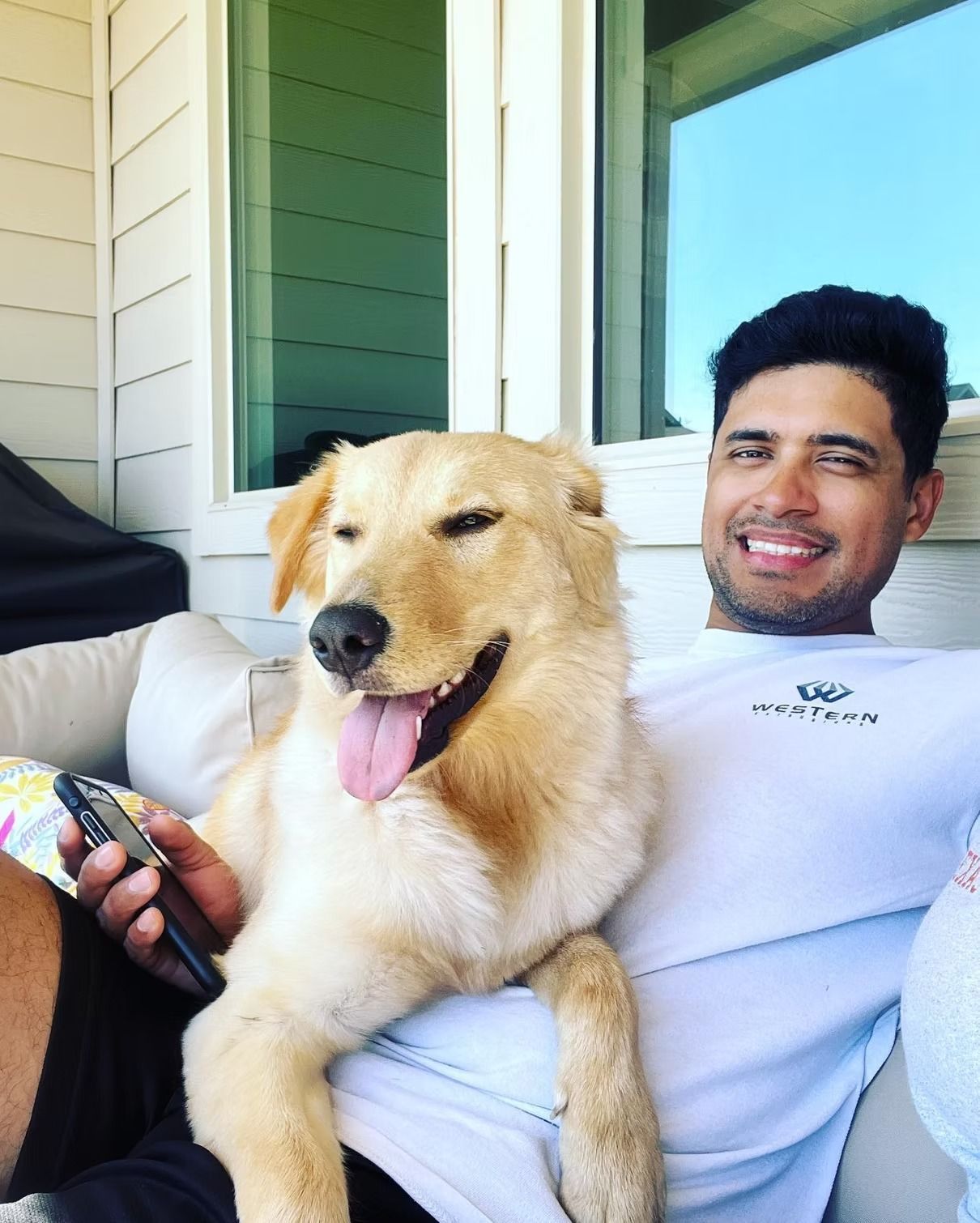 Man with tan dog, both smiling, sitting on a couch outdoors. Sunny day.