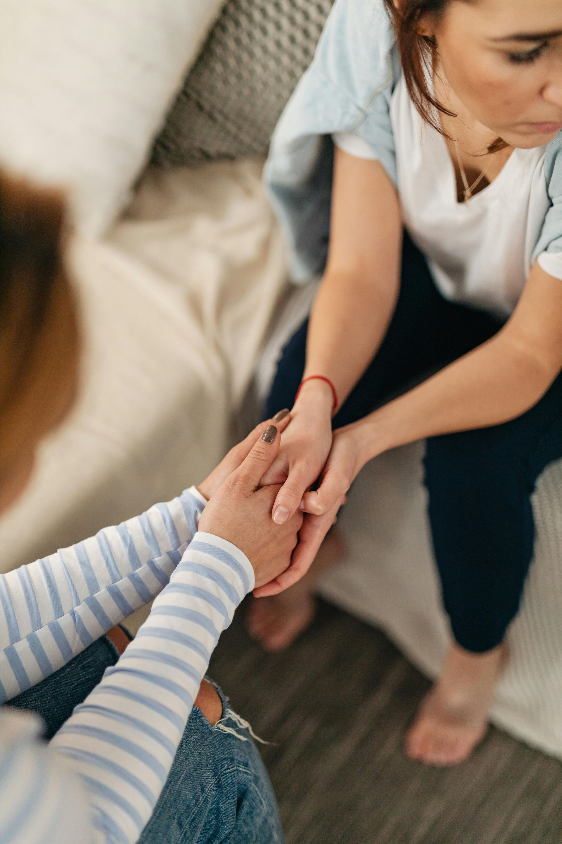 Two people holding hands indoors, one comforting the other on a couch