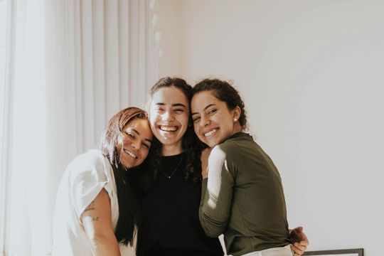 Three smiling people standing close together indoors, posing for a group photo.