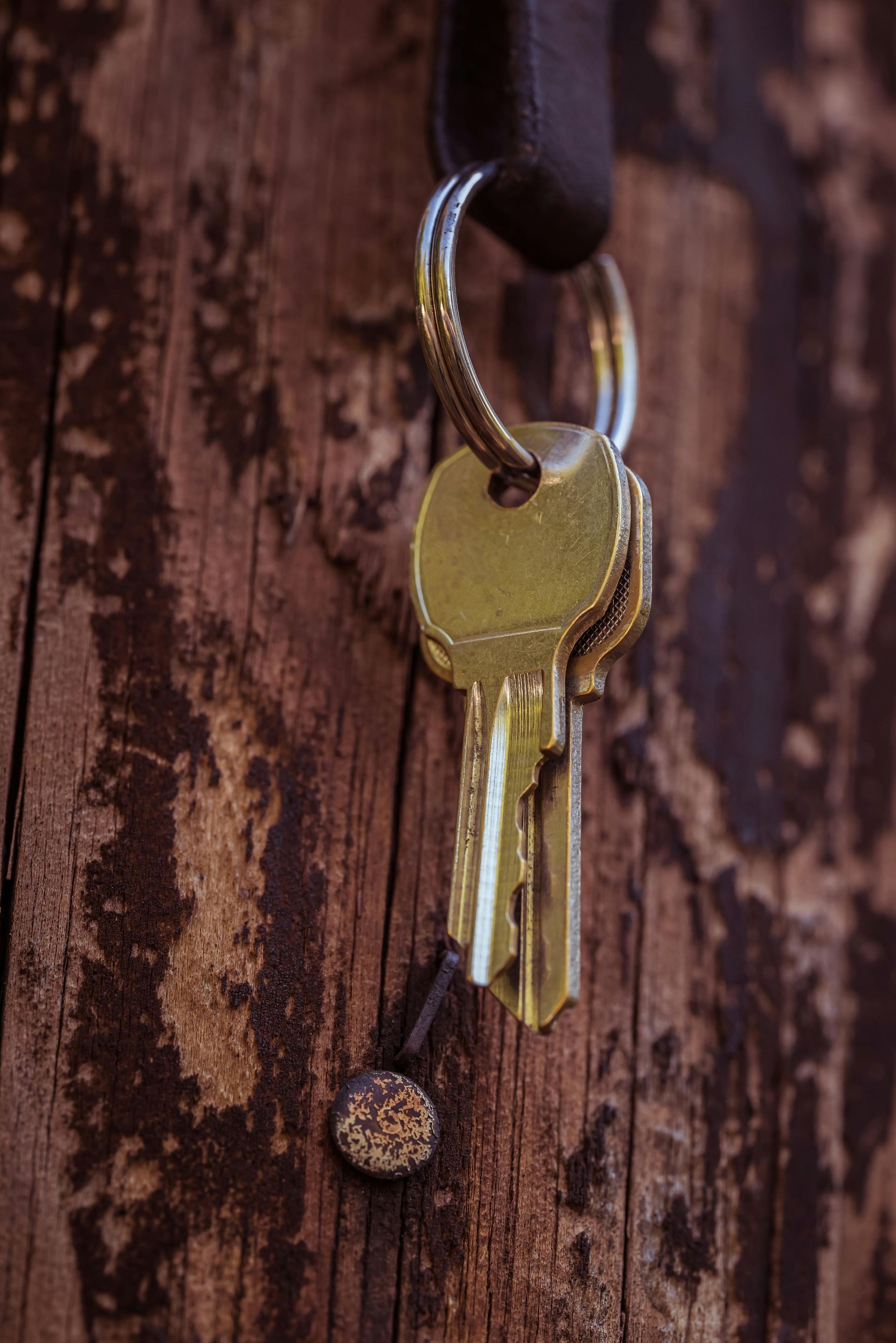 Old brass key hanging from a key ring against a weathered wooden surface