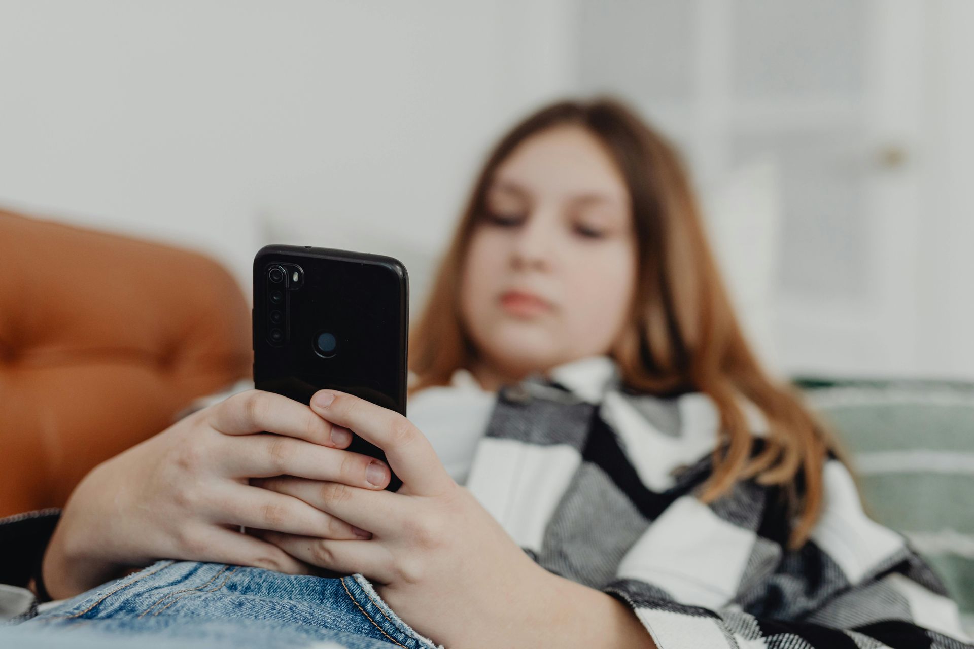 Person lounging on a couch, looking at a smartphone with a black-and-white blanket over their lap.