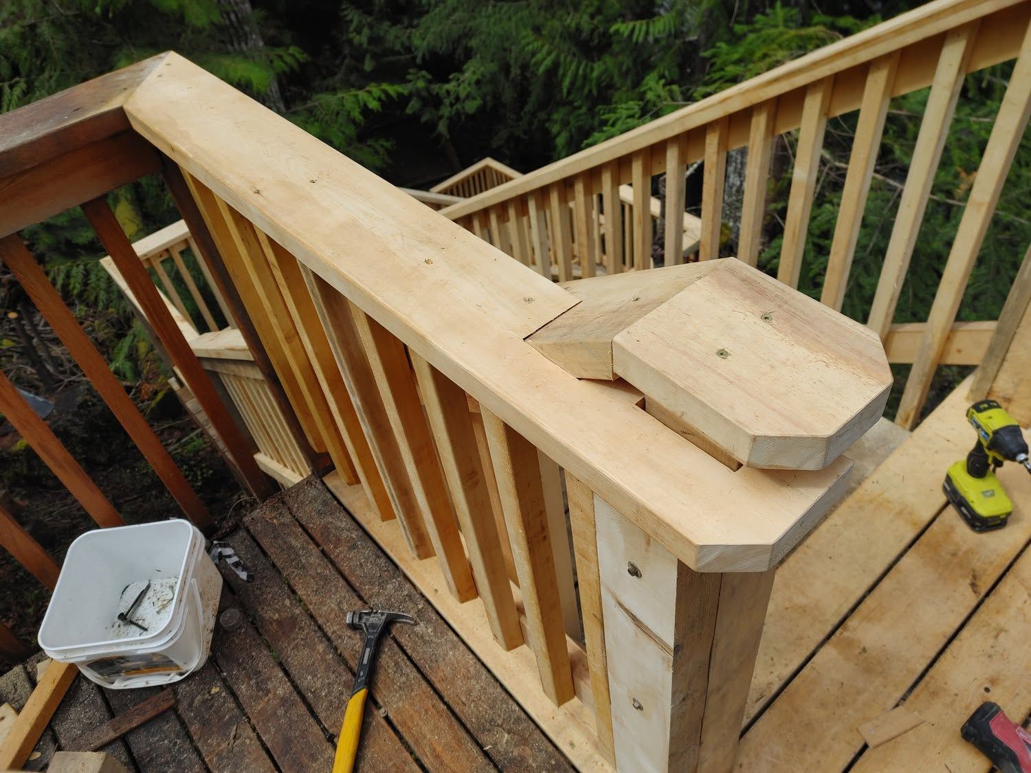 Wooden deck staircase under construction with new railings, tools, and a covered bucket on the steps