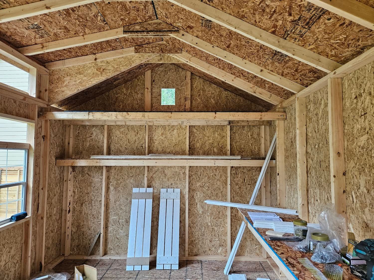 Partially built wooden shed interior with exposed framing, workbench, and stored materials
