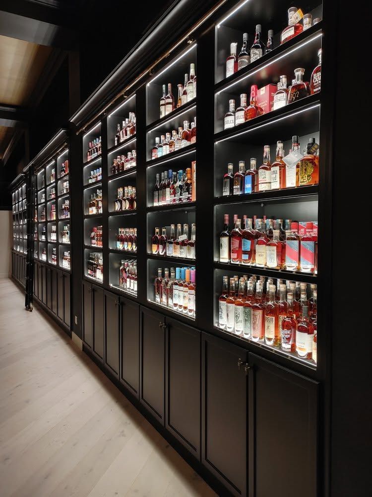 A sleek bar wall with backlit shelves of liquor bottles in a dark hallway