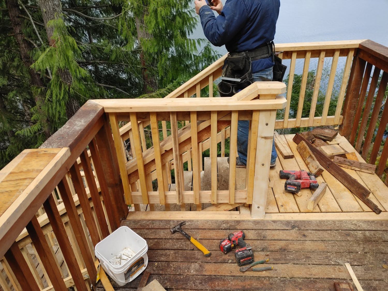 Person installing a wooden deck railing with tools on the unfinished deck overlooking water